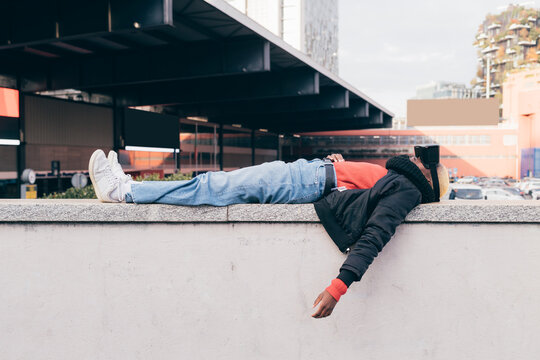 Italy, Woman with VR goggles lying on wall in city