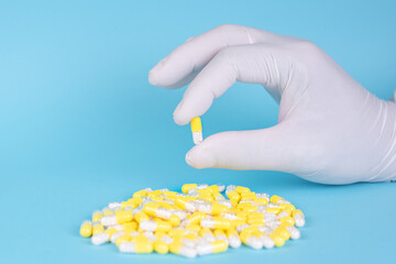 hand with surgical glove taking yellow capsules or pills with white lozenges medicine on blue background