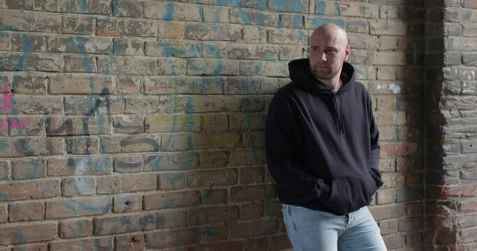young caucasian american man in black hoodie wear standing at street waiting for victim to commit a crime. cruel bearded european man outdoors at daytime. Concept portrait of dangerous criminal