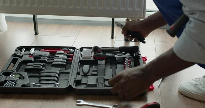 black professional plumber worker installing heating radiator in an empty room of a newly built apartment or house, taking tools instruments. Construction, maintenance and repair concept.