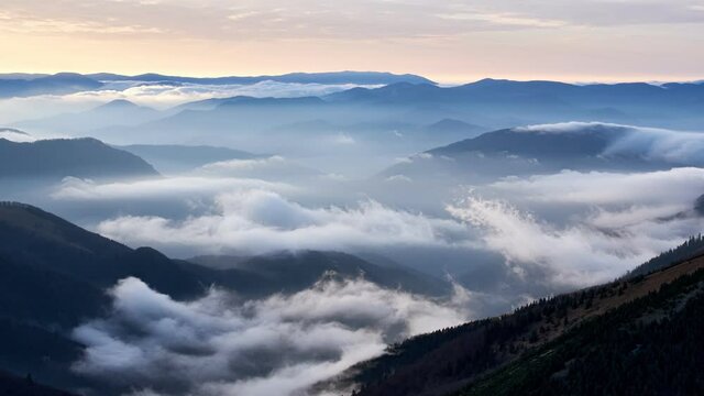 Clouds spill over the tops of the hills in the light of the rising sun, Mystical Atmosphere