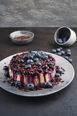 Traditioneller Heidelbeeren Käsekuchen mit frischen Beeren, Kompott und Schokoladenstreuseln serviert als close-up auf einem Design Teller mit Textfreiraum