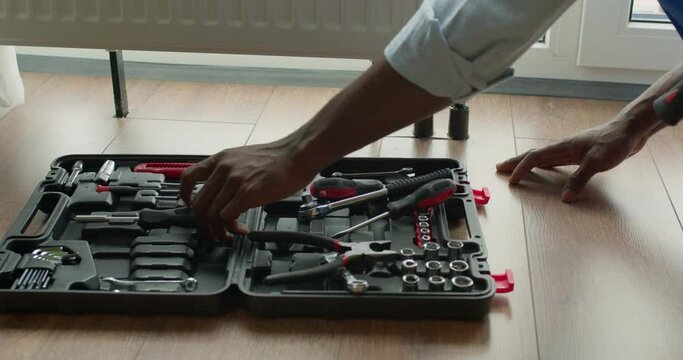 Black professional repair man is repairing radiator battery in the room. Maintenance repair works renovation in modern flat. Heating restoration. Wrench in hands, using tools. service male at work