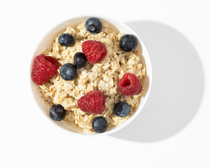 oatmeal with raspberries and blueberries in white bowl on white table. Top view.