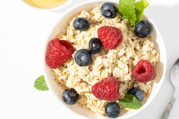 oatmeal with raspberries and blueberries in white bowl on white table. Top view.