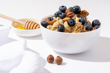 Bowl of oatmeal porridge with blueberry and nuts on white table. Healthy breakfast and diet food