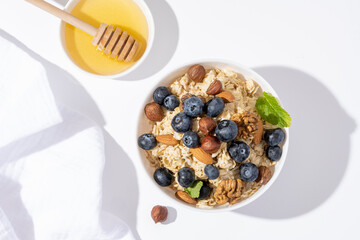 Bowl of oatmeal porridge with blueberry and nuts on white table top view. Healthy breakfast and diet food