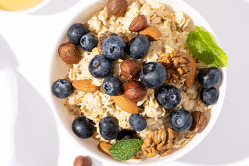 Bowl of oatmeal porridge with blueberry and nuts on white table top view. Healthy breakfast and diet food