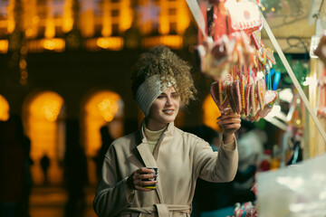 A portrait of a beautiful young woman holding a cup of mulled wine to warm up on the street with Christmas decorations.