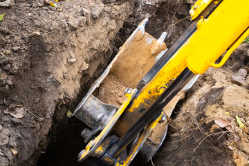 The excavator bucket digs a deep hole. Earthworks for the installation of plumbing pipes and septic...