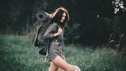 Hiking. A young girl with a retro backpack for hiking walks along a clearing road. Hitch-hiking