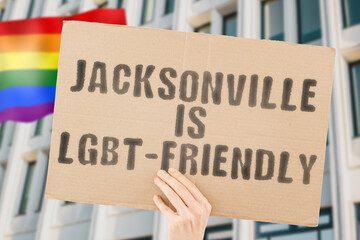 The phrase " Jacksonville is LGBT-Friendly " on a banner in men's hand with blurred LGBT flag on the background. Human relationships. different. Diverse. liberty. Sexuality. Social issues. Society