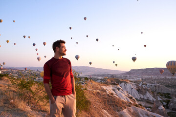 Tourist man standing and looking to hot air balloons in Cappadocia, Turkey.Happy Travel in Turkey concept.Traveler on a mountain enjoying view of hot air baloons