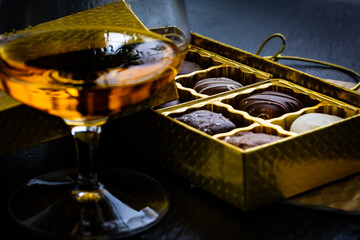 Close up of a box of chocolate candies in golden box behind brandy glass