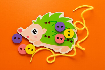 Wooden game lacing hedgehog. Wooden hedgehog, wooden buttons and lace on an orange background. Montessori toys, the development of fine motor skills, logic, the study of colors.