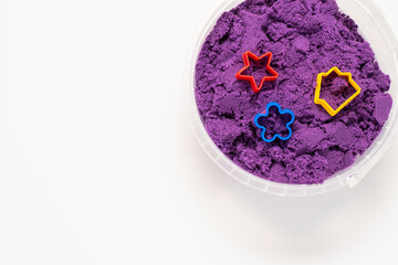 Container with lilac kinetic sand and molds for modeling on a white background. Top view, place for text, copy space.