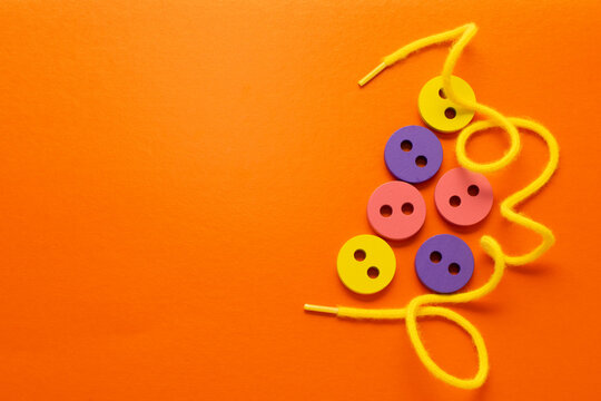Wooden buttons and yellow lace on an orange background. Montessori toys, lacing game, development of fine motor skills, logic, learning colors. Copy space, place for text