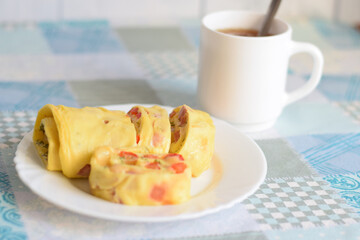 Egg omelette roll on a white plate and a cup of tea on the table. Delicious healthy breakfast....
