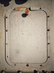 Rusty steel hatch door secured with nuts and bolts