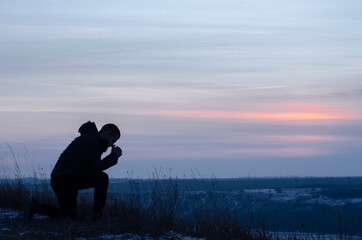 Prayer. Repentance. A man on his knees. Prayer. Silhouette of a man on a blue sky background....