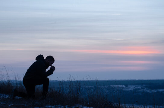 Prayer. Repentance. A man on his knees. Prayer. Silhouette of a man on a blue sky background. Kneeling Prayer to God. Glorification. Praising God. Christian