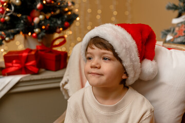 A child with Santa Claus hat sits in front of the Christmas tree
