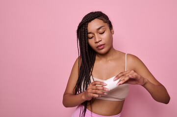 Fototapeta na wymiar Close-up beauty portrait on pink background of African woman with dreadlocks in beige underwear holding antiperspirant in her hands. Purity, hygiene, body care concept. Copy space