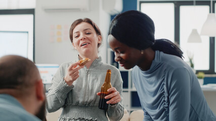 Group of colleagues having fun with drinks after work. Workmates enjoying bottles of beer and pizza while playing at foosball game table for entertainment. Coworkers after hours