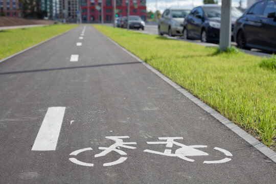 New empty bicycle path closeup with green grass and cars around. White bike symbol on road. Bicycle infrastructure in the city. Bikeway with no people. Separated road for cycling.