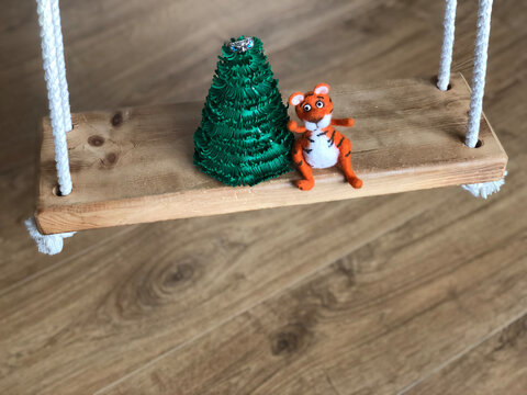 handmade toy tiger made of wool sits nearby christmas tree  on a wood swing and dream  close up. Funny festive vintage background top view