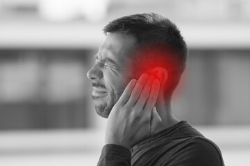 Young man suffering from of strong earache or ear pain. Ear diseases - obrazy, fototapety, plakaty