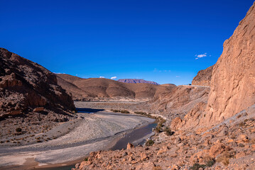 Dried-up river through mountains against clear sky on sunny summer day, dry river flanked by mountains
