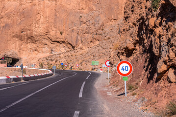 Winding mountain road with speed limit signs through rock formations, Curvy road with signs through...