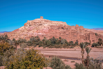 Green plants with historic fortress structure and rocky hill against clear blue sky