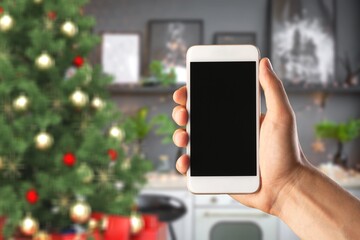 Human holding smartphone in hands using cell phone mockup blank screen on Christmas tree background
