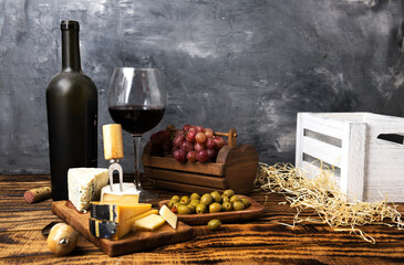 Red wine in a dusty bottle and glass. Grapes and olives with cheese on a wooden table