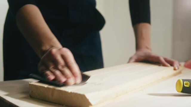 Woman builder sanding wooden board with sandpaper. Female carpenter improving wood surface, making diy furniture. Renovation concept. Building new house or flat.