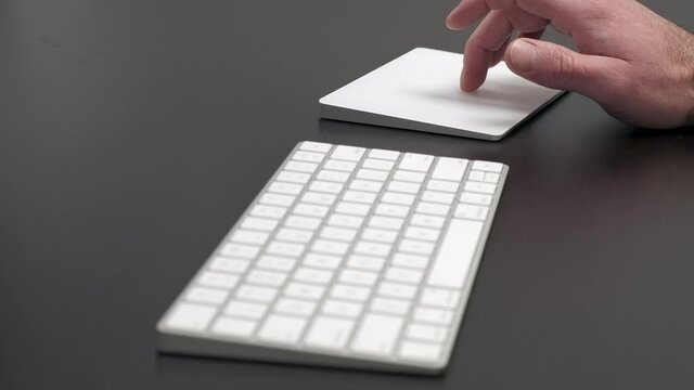 Man using Apple Magic Keyboard and Magic Trackpad sitting at a desk to scroll and select.