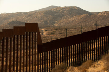 Tecate, Baja California, Mexico - September 14, 2021: Late afternoon sun shines on the USA Mexico border wall as it winds through Tecate.