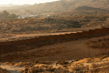 Tecate, Baja California, Mexico - September 14, 2021: Late afternoon sun shines on the USA Mexico border wall people walk in front of it.