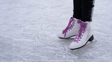 Legs of a girl in white figure skates with purple laces on an outdoor skating rink in the park.