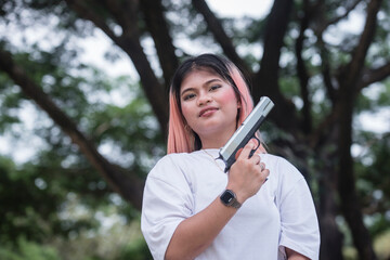 A smug young woman holding a gun while outdoors. A gun advocate or flaunting a dangerous weapon.