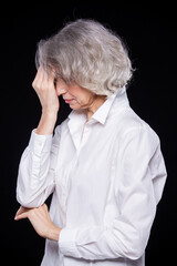 Side view portrait of an old but modern trendy woman suffering from a headache or migraine holding her head in her hands with a desperate expression isolated on black background