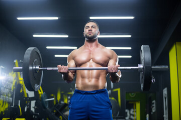 Fototapeta na wymiar Close up view of a strong muscular athlete lifting heavy barbell showing his muscles in a gym