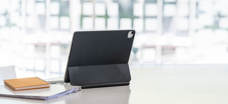 Portable tablet and notebook on wooden table in modern office room with copy space.