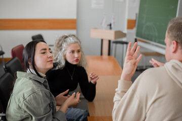 Two girls and a guy are talking in sign language. Three deaf students chatting in a university classroom.