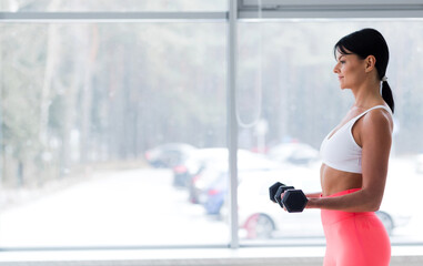 Girl posing with dumbbells in front of the window