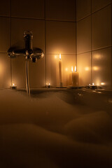 Romantic bathroom with white foam by candlelight in the dark