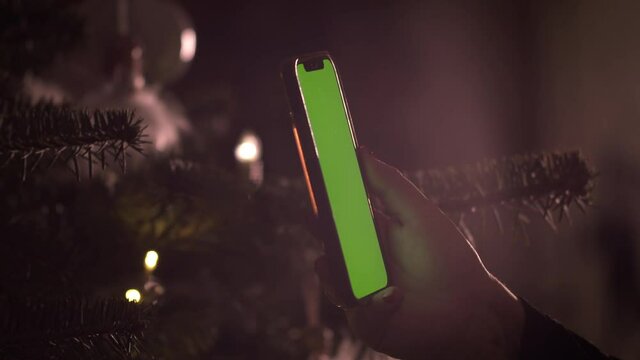 Woman Hand Swipes Green Screen Smartphone By Christmas Tree, Close Up