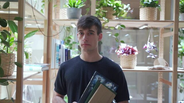 Portrait of blach hair male student stands holding books in the library. Green scandinavian organic background.